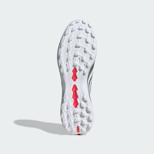 Bottom view of a white athletic shoe sole with prominent lug pattern and red midfoot inserts on a pale background