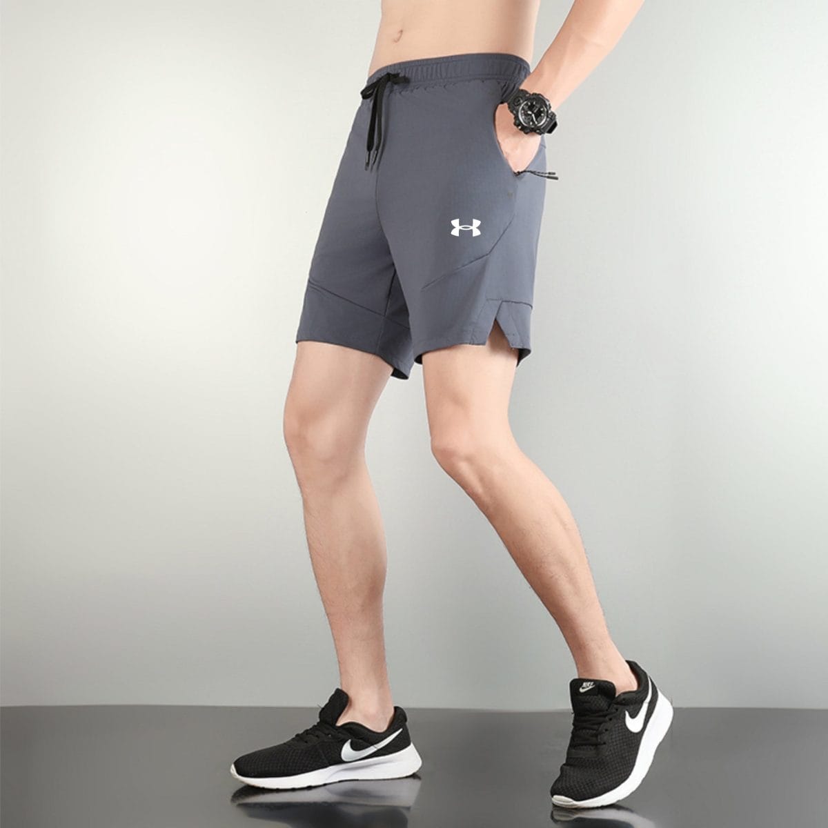 Lower body of a person walking on a treadmill wearing gray athletic shorts and black Nike sneakers, with a black wristwatch visible on the left wrist.