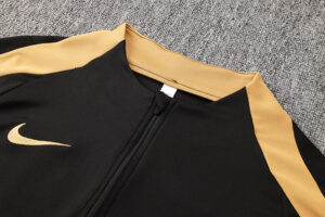 Black zip-up athletic jacket with gold side panels and a gold Nike swoosh on the left chest.