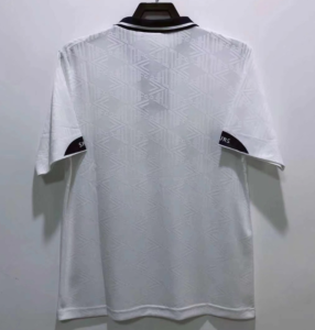 White polo shirt hanging on a hanger, shown from the back, featuring a subtle geometric pattern and a black-trimmed collar against a plain wall.