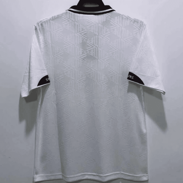 White polo shirt hanging on a hanger, shown from the back, featuring a subtle geometric pattern and a black-trimmed collar against a plain wall.