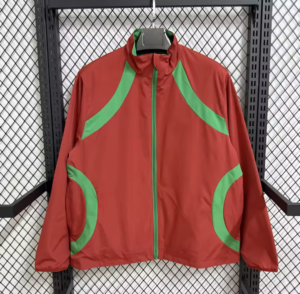 Red windbreaker with green curved panels on shoulders and pockets, hanging on a rack.