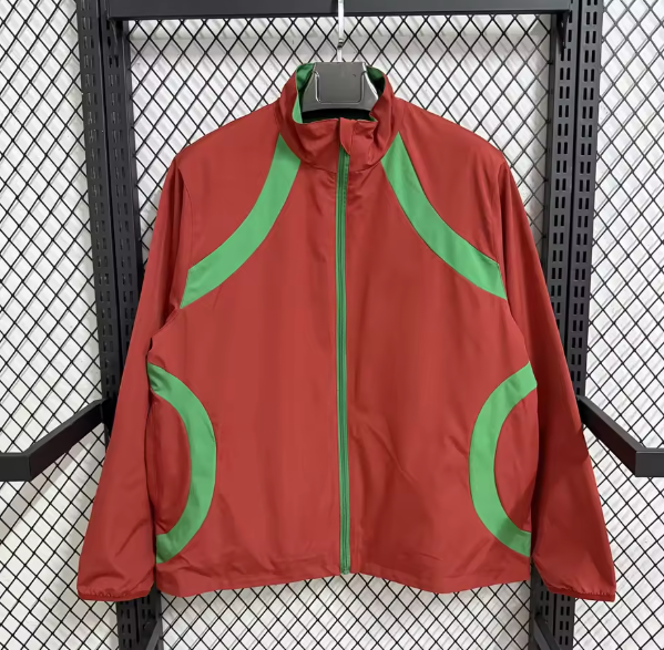 Red windbreaker with green curved panels on shoulders and pockets, hanging on a rack.