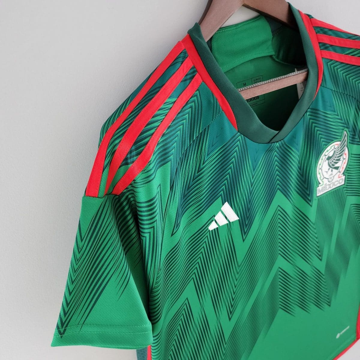 Close-up of a green patterned sports jersey with red stripes on a hanger, showing fabric texture and a badge partially visible.