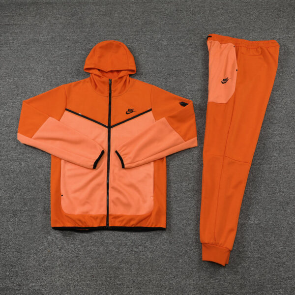 Orange color-block Nike tracksuit jacket with peach panels and matching orange jogger pants laid out on a gray surface.