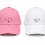 12d0c73f-c8f9-4a00-81c5-0a41f2d3f90d | UAE SPORT STORE Two Prada baseball caps side by side: pink on the left and white on the right, each with a triangular logo patch on the front.