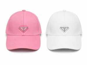 Two Prada baseball caps side by side: pink on the left and white on the right, each with a small triangular Prada logo on the front.
