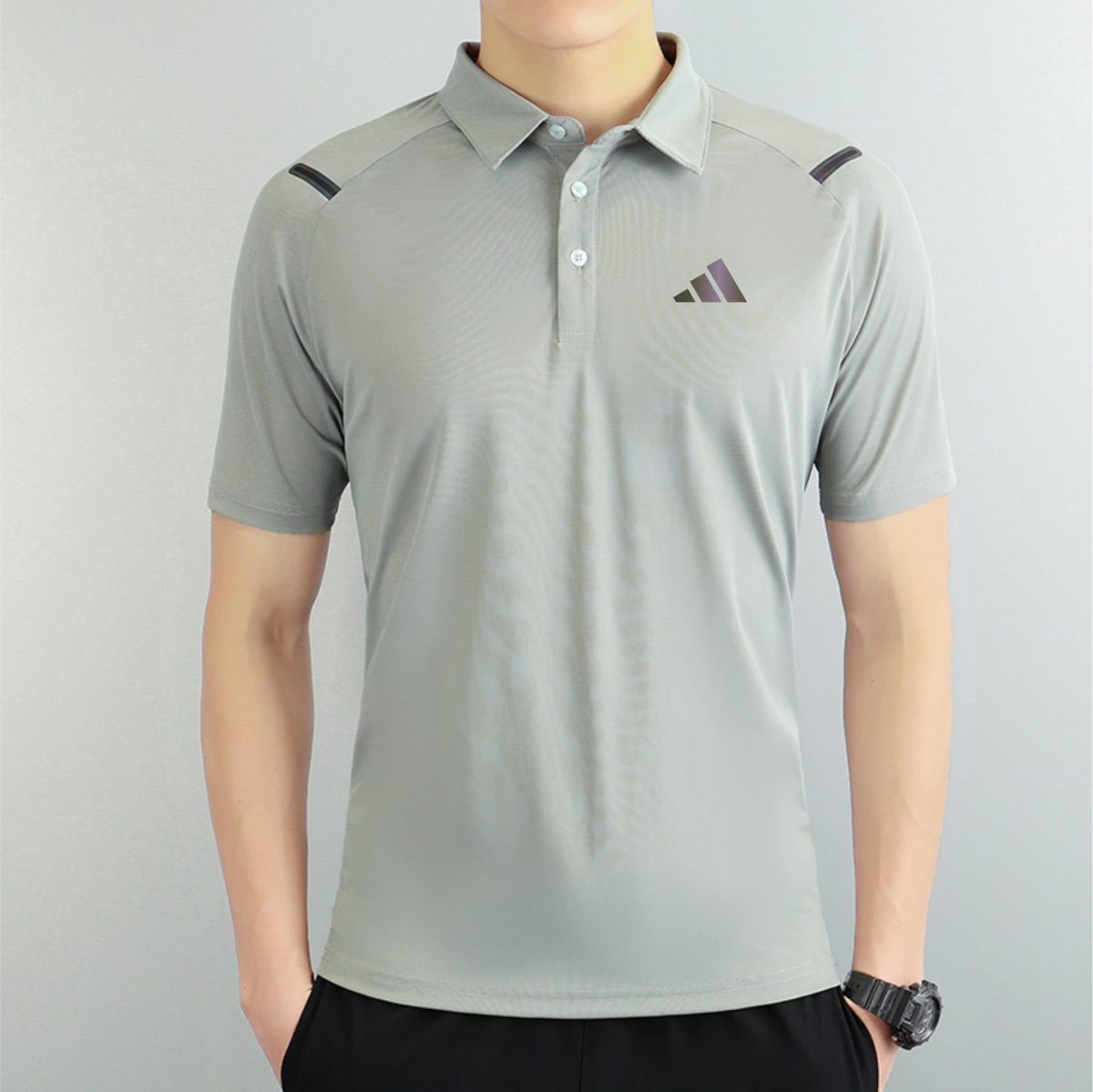 Person wearing a light gray polo shirt with a small purple gradient logo on the left chest, and a black watch on the right wrist.