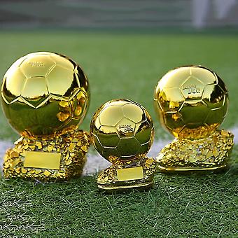 Three gold soccer ball trophies of different sizes on a grassy field.
