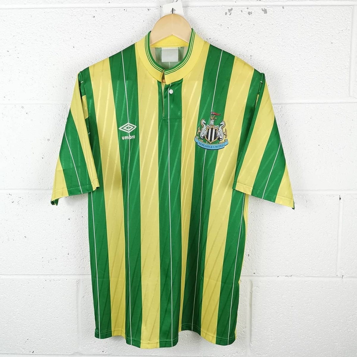 Newcastle United football jersey with green and yellow vertical stripes and club crest on the left chest, hanging on a hanger