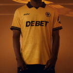 Person wearing a yellow soccer jersey with a black collar, sponsor text 'DEBET' across the chest, and a team crest on the left