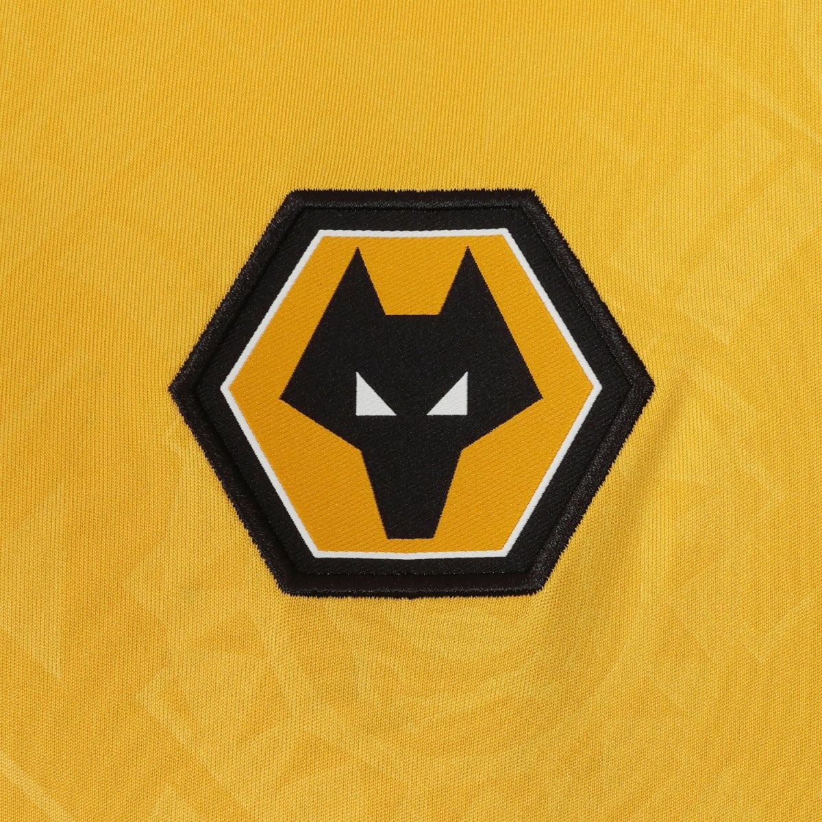 Embroidered Wolverhampton Wanderers crest on a yellow jersey, showing a black wolf head inside a gold and black hexagonal badge.