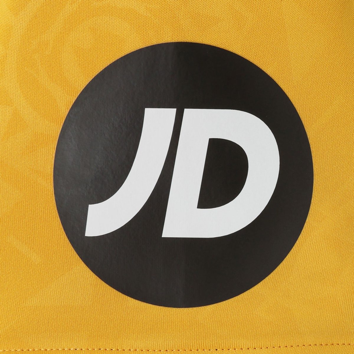 Close-up of a black circular logo with white 'JD' on yellow fabric background.