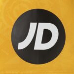 Close-up of a black circular logo with white 'JD' on yellow fabric background.