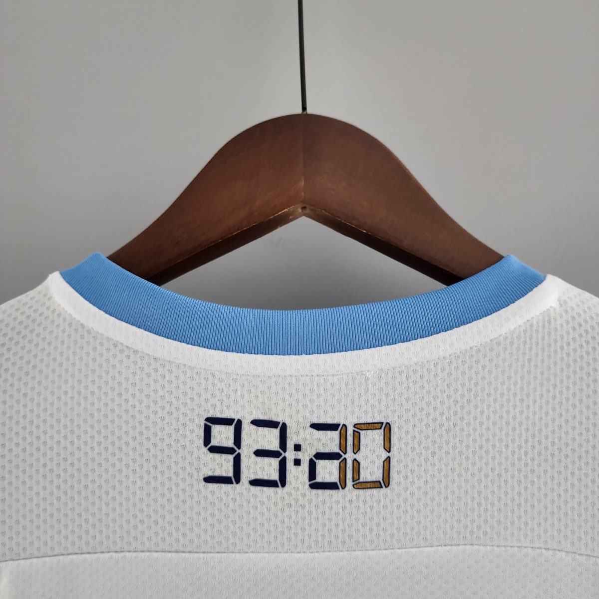 Wooden clothes hanger holding a light blue-collared shirt photographed from the front.