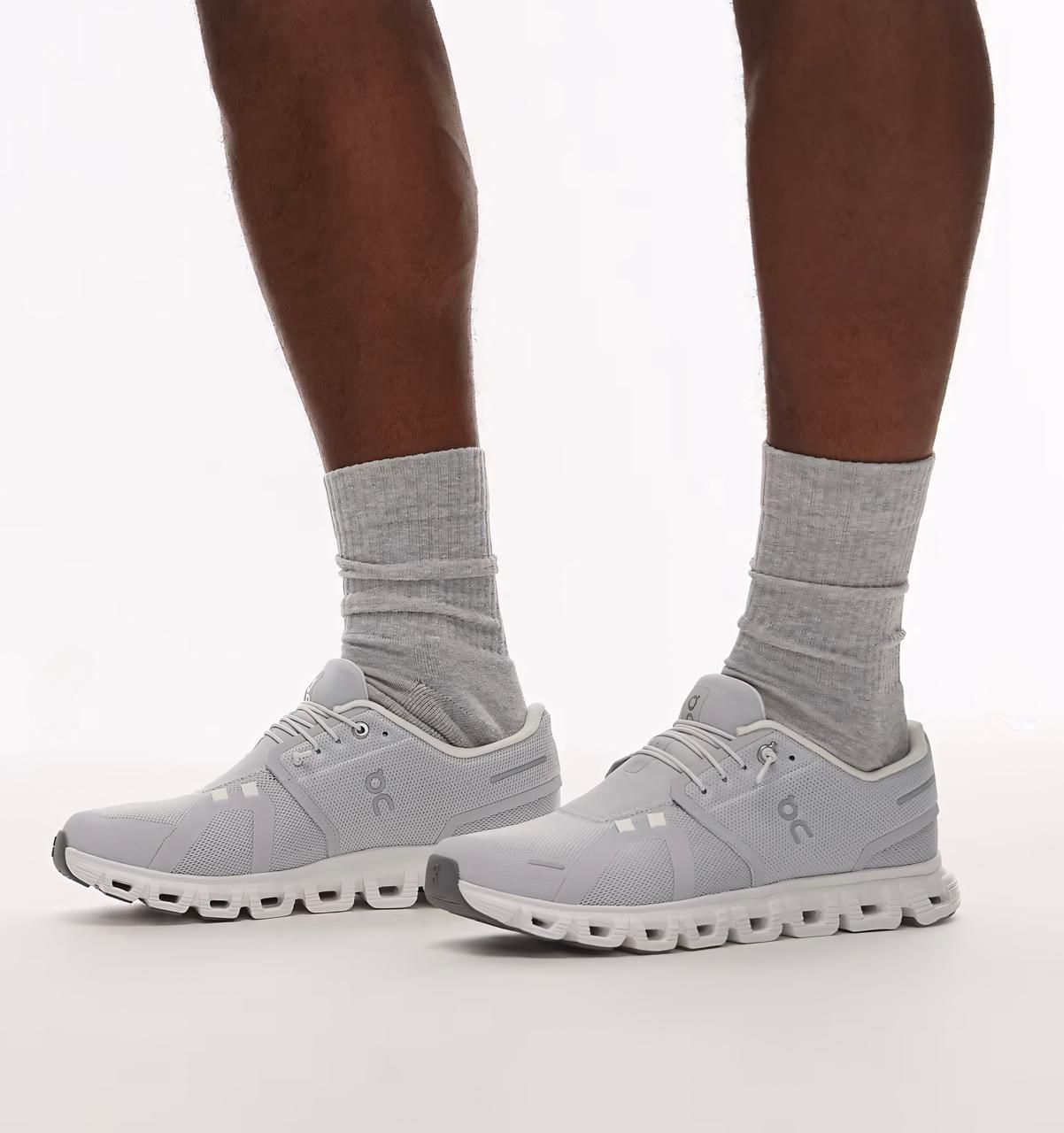 136456e0-39a2-4f47-97f7-39e926b341e0 | UAE SPORT STORE Light gray running shoes with thick white soles worn with gray crew socks, standing on a white background.