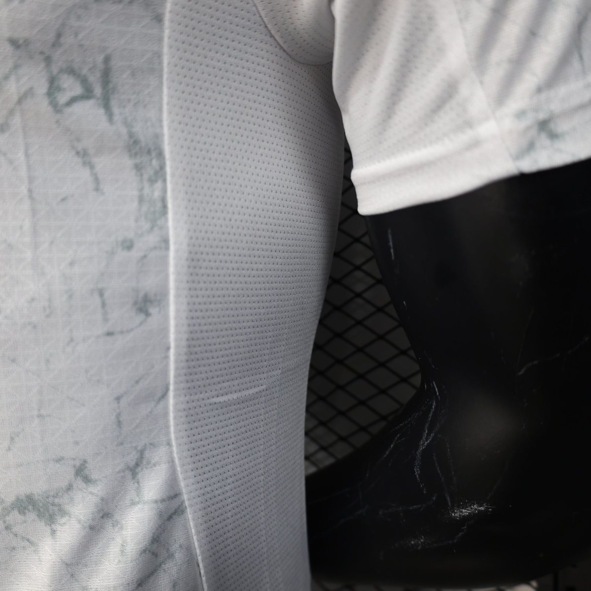 Close-up of two gray fabrics meeting at a seam: one textured with small perforations and a marbled light-gray pattern nearby, against a dark glossy surface and a mesh background.