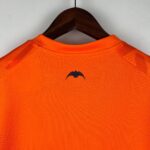 Bright orange textured polo shirt hanging on a wooden hanger, viewed from the back against a gray wall.