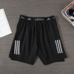 Black Adidas athletic shorts with an elastic waistband and white three-stripe accents on each leg, shown in flat lay.