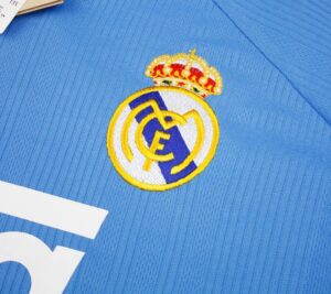140273f6-0db3-44a9-a932-93c019bf0348 | UAE SPORT STORE Embroidered Real Madrid crest on a blue jersey fabric, close-up detail
