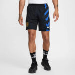 Man wearing black athletic shorts with blue chevron stripes, a club crest on the left leg, and a white Nike swoosh on the right leg, paired with black socks and sneakers.