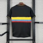 Black T-shirt on a hanger with yellow, blue, and red horizontal stripes across the chest, displayed on a metal garment rack.