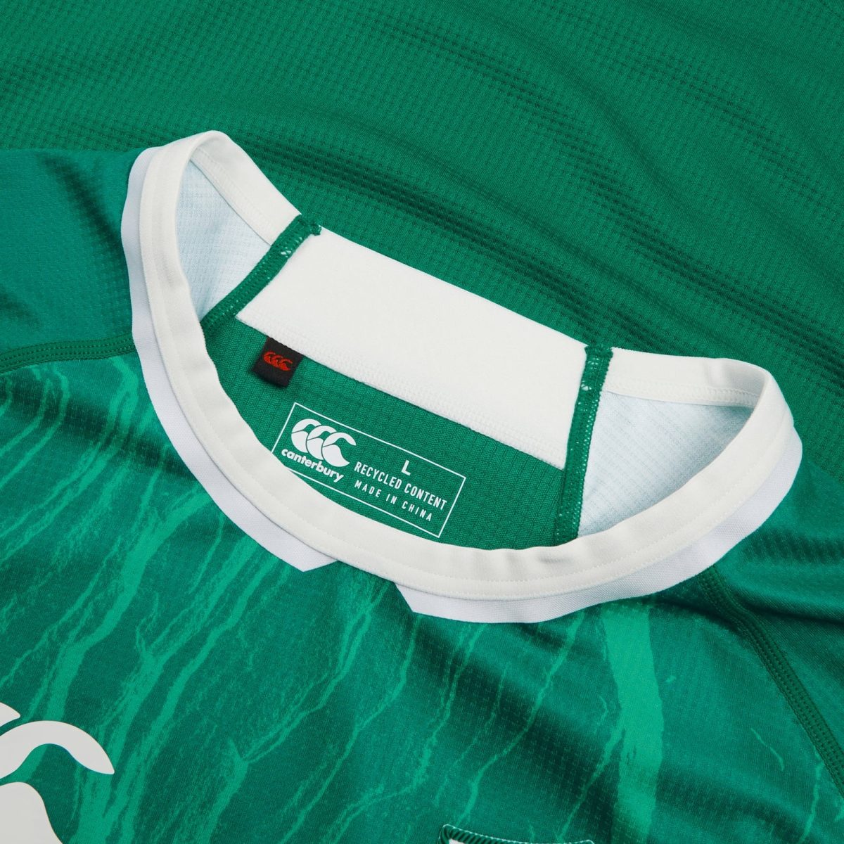 Close-up of a green rugby jersey collar with white trim and a Canterbury label reading 'recycled content made in China'