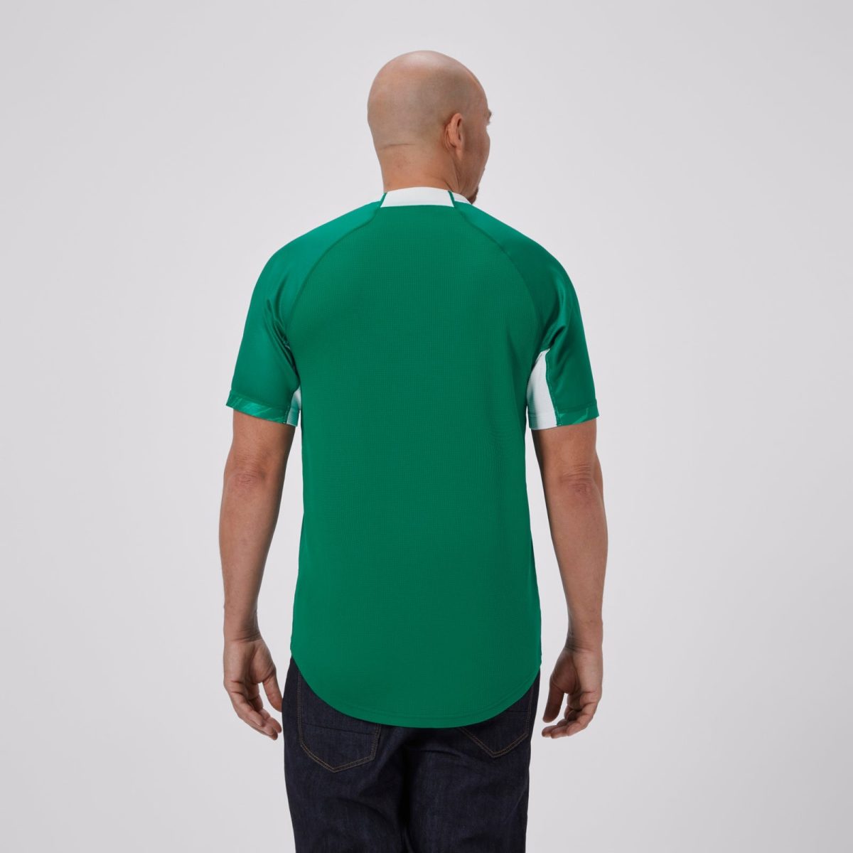 Back view of a man wearing a green polo shirt with a white collar, standing against a light gray background.