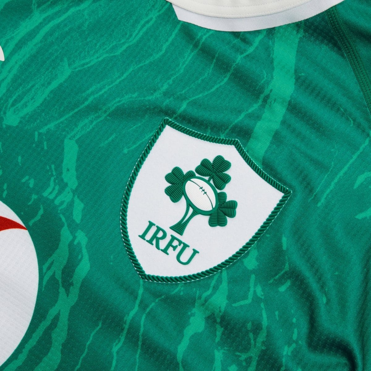 Close-up of the IRFU logo on a green jersey, showing a white shield with a green shamrock and rugby ball details.