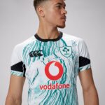 Man wearing a white teal-patterned rugby jersey with IRFU crest, Vodafone logo, and CCC emblem, looking to the right.