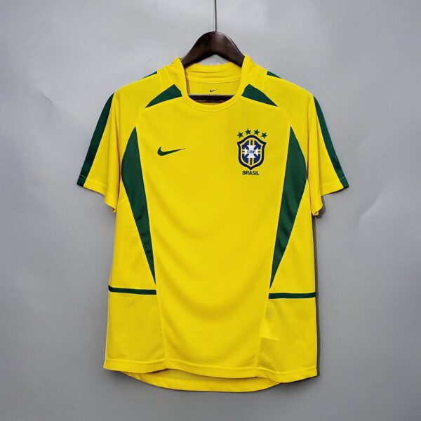 Yellow Brazil national football team jersey on a hanger, with green accents and team crest visible on the chest against a plain gray wall.