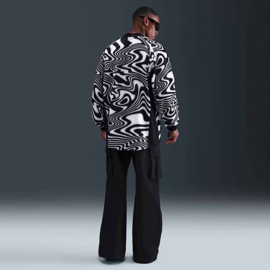 14b61f0f-954c-4e7f-9061-ba59d80ffb49 | UAE SPORT STORE Back view of a man wearing a bold black-and-white swirling-pattern shirt and black wide-leg pants, with sunglasses on.