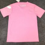 Pink T-shirt laid flat on a gray surface, back neckline shows white Arabic text 'المفكر'.
