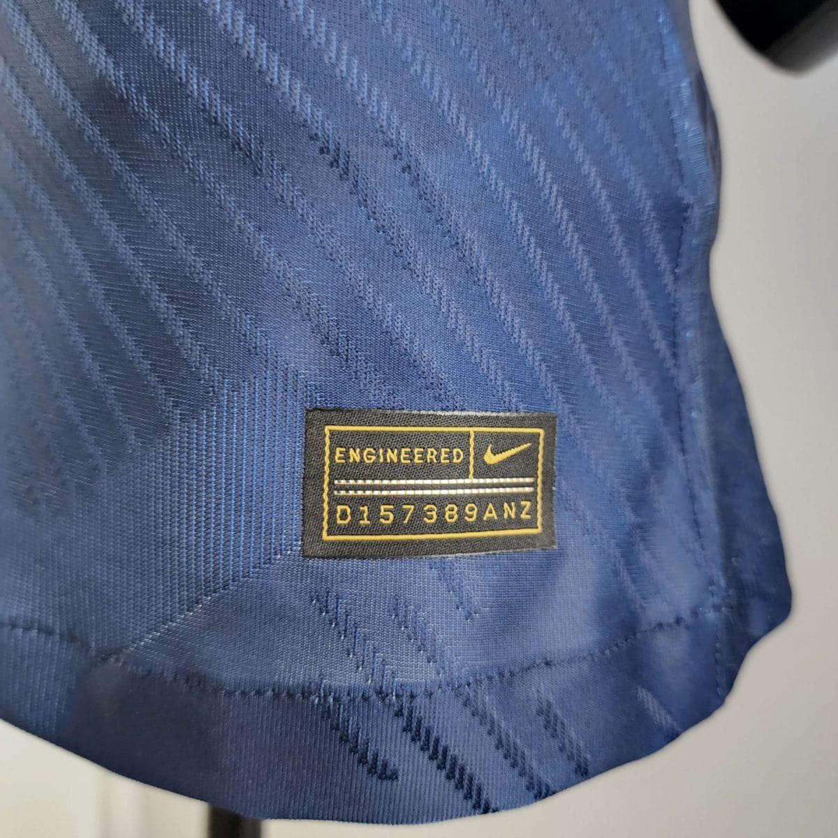 Close-up of blue woven fabric with a black-and-yellow rectangular patch that reads 'ENGINEERED' and a serial code beneath it.