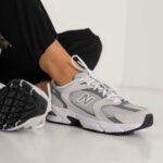Person tying the white-and-gray New Balance sneaker on their foot, laces being tightened.