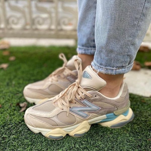 Beige chunky sneakers on a person standing on artificial grass, jeans cuffs rolled up.