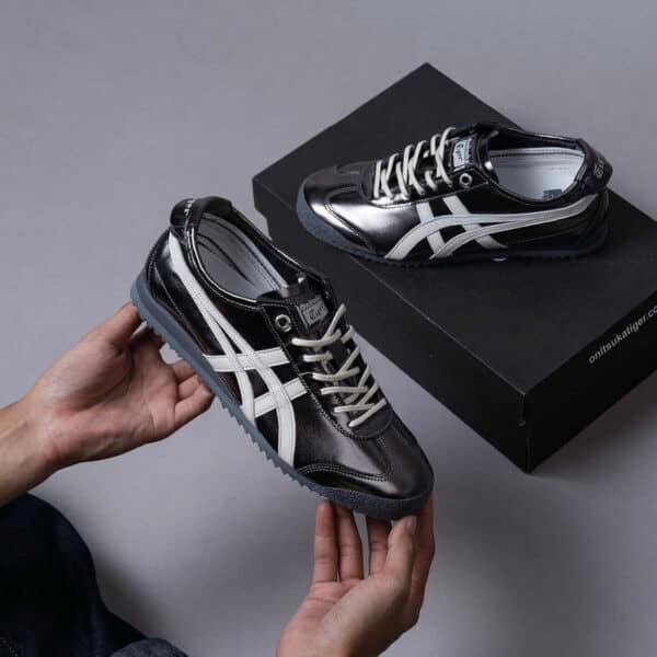 Black glossy sneakers with white stripes held in hands, a black shoebox in the background (Onitsuka Tiger style).]