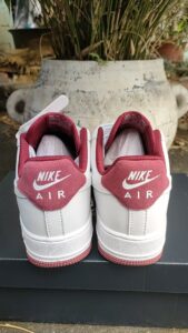 Pair of white Nike Air sneakers shown from the back with red heel tabs against a dark display surface.