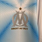 1668e63c_d82c331e-9d8e-4a56-b0db-e7dbd306fb3c | UAE SPORT STORE Blue fabric with a silver trophy emblem and a small star above, with partial text 'DROIT AU BUT' at the bottom.