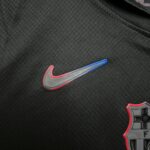 Close-up of dark woven fabric with a partial view of a gray item featuring red and blue stitching at the bottom-right corner.
