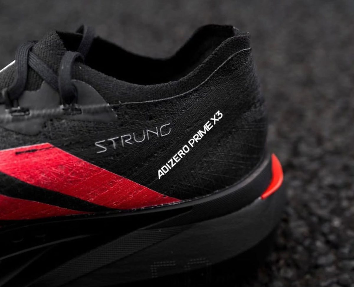 Black athletic heel of a running shoe with red stripe, showing the words 'STRUNG' and 'ADIZERO PRIME X' on the side.