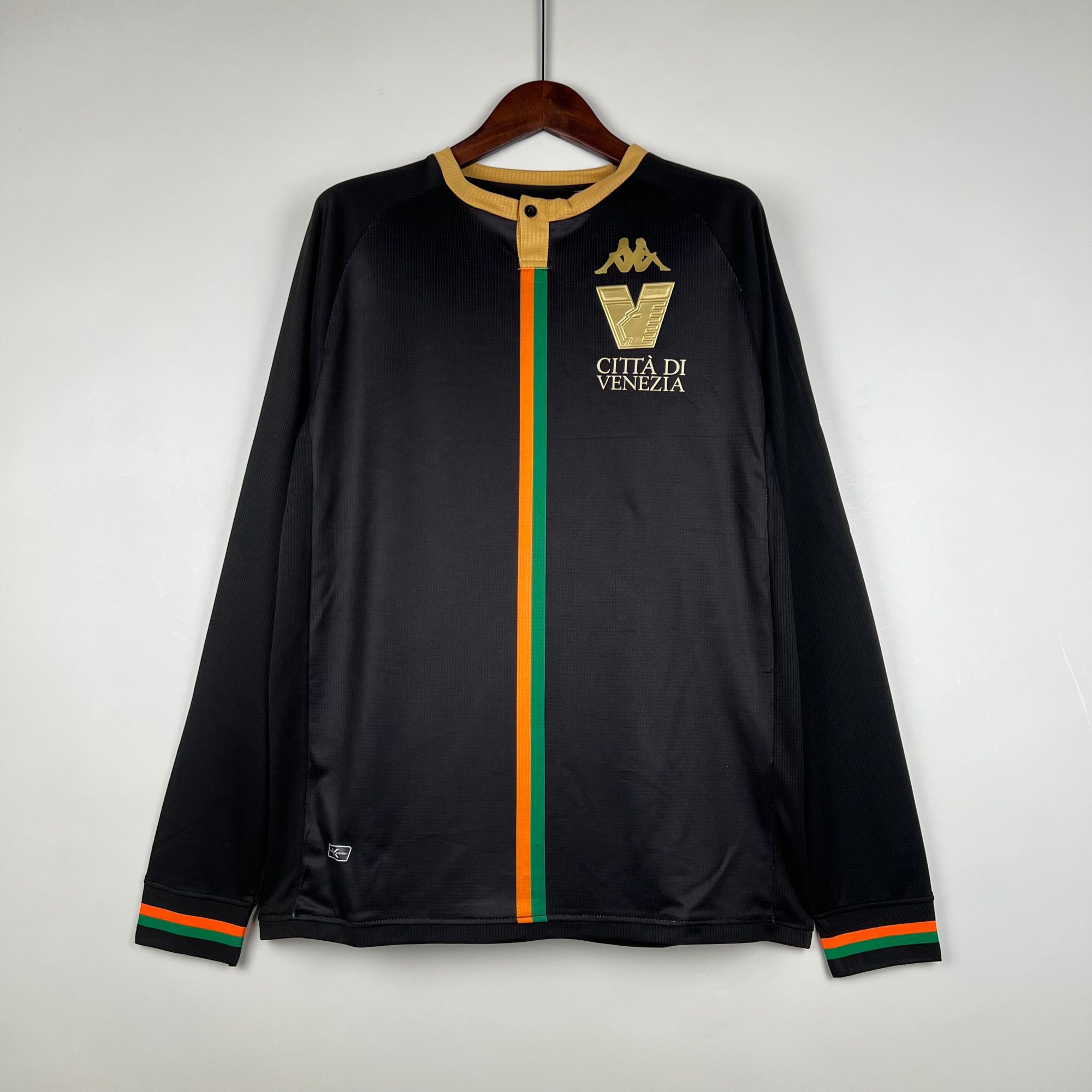 16f71918 | UAE SPORT STORE قميص رياضي أسود على علاقة بخط عمودي برتقالي وأخضر وشعار مدينة فينيتسيا الذهبي، على خلفية فاتحة.