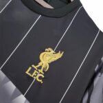Close-up of a dark jersey with white piping and a gold embroidered Liverpool FC crest.