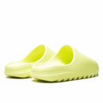 Close-up of lime-green slip-on sandals with wide, curved straps on a white background.