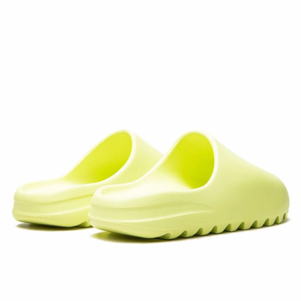 Close-up of lime-green slip-on sandals with wide, curved straps on a white background.