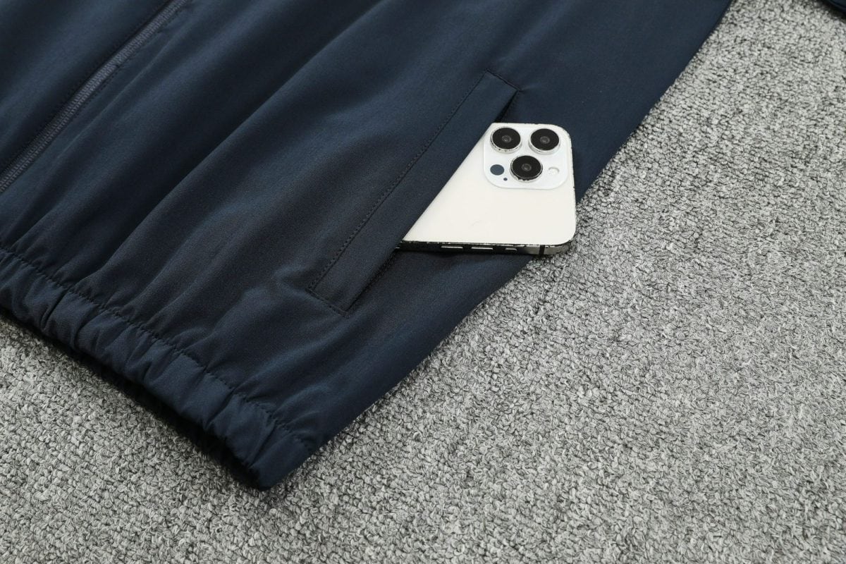 White iPhone with triple camera peeks from a navy jacket pocket on a gray carpet.