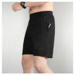 Model wearing black athletic shorts with a zippered side pocket and a small Under Armour logo, shown in a side view.