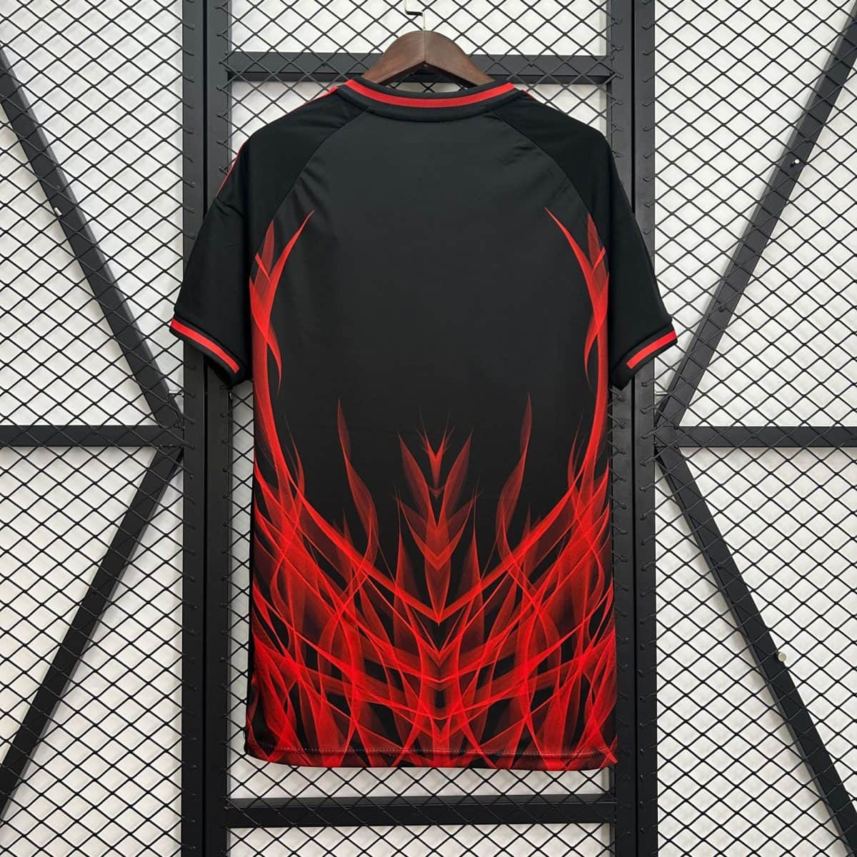 Black jacket with bright red flame graphic hanging on a wooden hanger against a metal mesh background