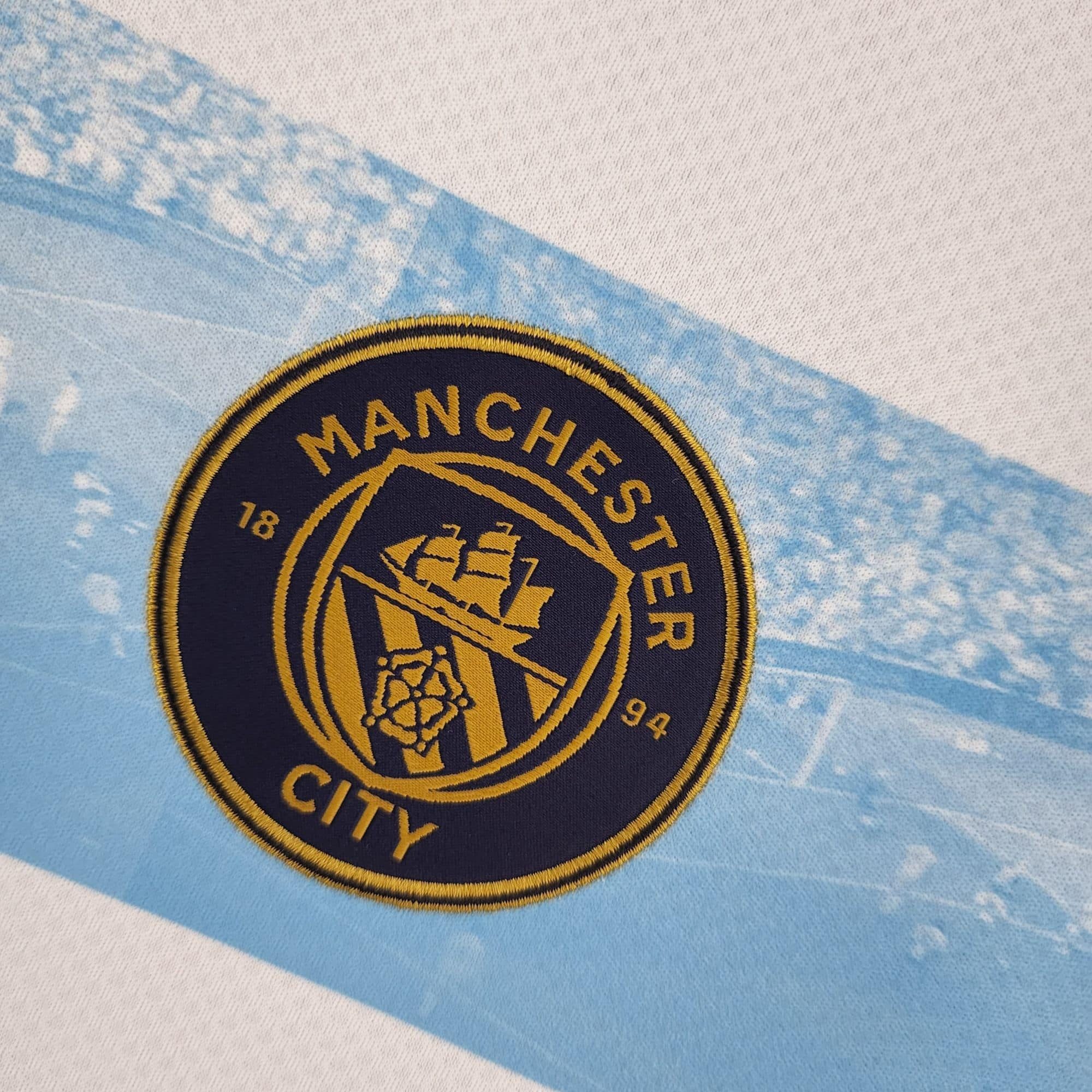 1754f9c3_76a52fbc-6ad2-408a-804d-26e36c906559 | UAE SPORT STORE Close-up of a navy circular patch with gold embroidery on a light blue tie-dye fabric background.