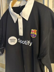 Black polo shirt with white collar and placket, featuring FC Barcelona crest on the left chest and a Spotify sponsor logo on the front